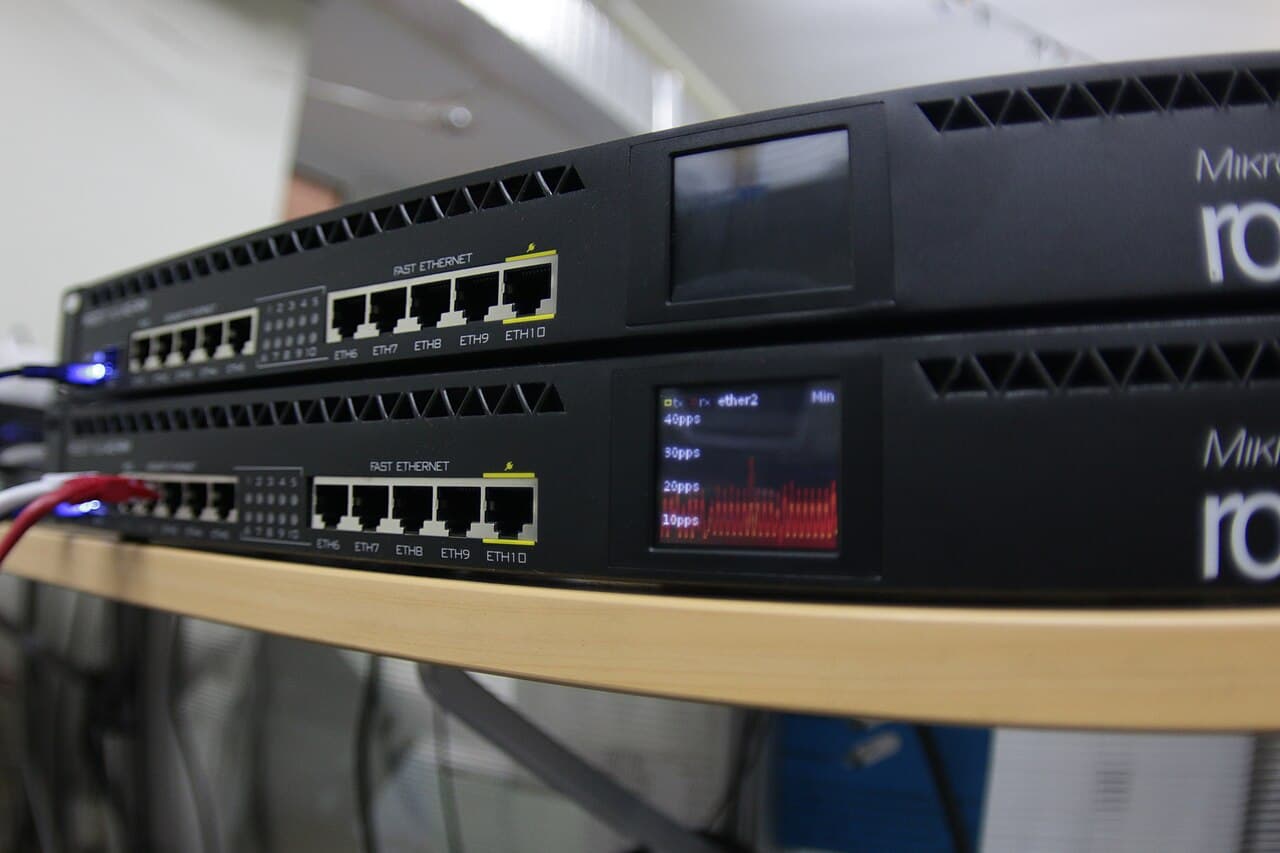 Two MikroTik rack-mount routers stacked, one screen showing a live traffic graph
